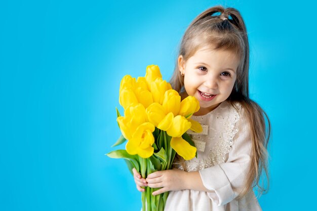 Portret van een lachend meisje een kind met een boeket gele tulpen op een blauwe geïsoleerde achtergrond Lifestyle International Women's of Mother's Day Ruimte voor tekst Hoogwaardige fotografie