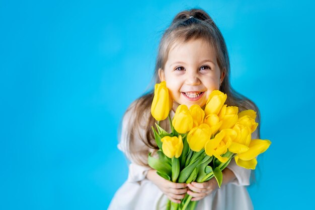 Portret van een lachend meisje een kind met een boeket gele tulpen op een blauwe geïsoleerde achtergrond Lifestyle International Women's of Mother's Day Ruimte voor tekst Hoogwaardige fotografie