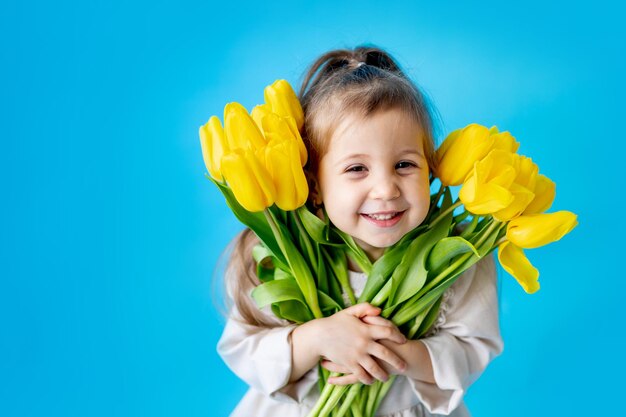 Portret van een lachend meisje een kind met een boeket gele tulpen op een blauwe geïsoleerde achtergrond Lifestyle International Women's of Mother's Day Ruimte voor tekst Hoogwaardige fotografie