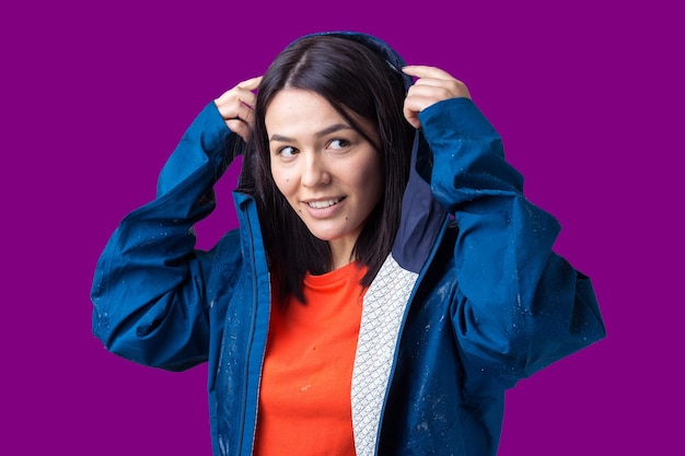 Portret van een lachend meisje gekleed in blauwe regenjas in druppels poseren met capuchon op grijze achtergrond in een studio