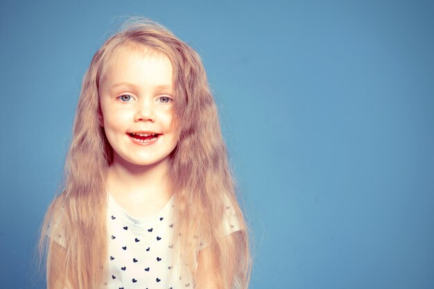 Portret van een lachend meisje met lang blond haar op een blauwe achtergrond in de studio