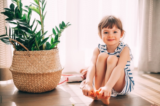 Portret van een lachend schattig klein meisje in gestreepte jurk, zittend op een vloer