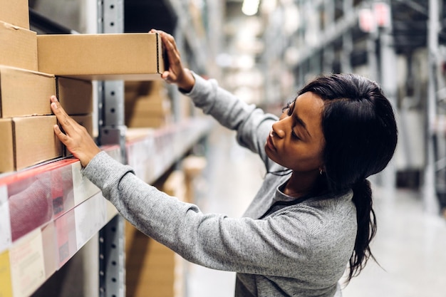 Foto portret van een lachende afro-amerikaanse zakenvrouw besteldetails die goederen en benodigdheden op planken controleren met goederenachtergrond in magazijnlogistieke en zakelijke export