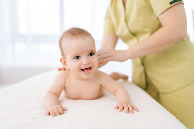 Portret van een lachende baby die een rugmassage krijgt, liggend op de buik van een professionele vrouwelijke masseuse. Gesneden foto van een jonge vrouwelijke therapeut die een massage uitvoert en spieren ontwikkelt.