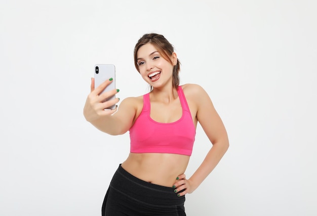 Portret van een lachende fitness vrouw met smartphone Selfie tijd op witte achtergrond