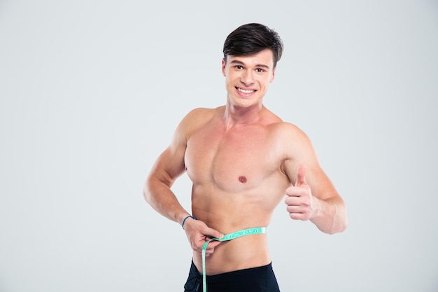 Portret van een lachende fitnessman die zijn lichaam meet en zijn duim omhoog laat zien