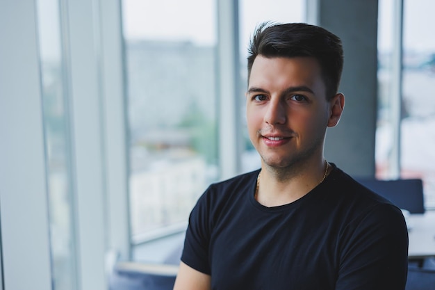 Portret van een lachende jonge man in een zwart t-shirt tegen de achtergrond van een modern kantoor stijlvolle man in vrijetijdskleding