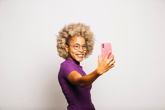 Portret van een lachende jonge vrouw die een smartphone gebruikt terwijl ze tegen een witte achtergrond staat