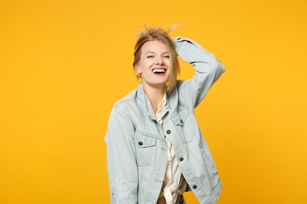 Portret van een lachende jonge vrouw in denim vrijetijdskleding die opkijkt en hand op het hoofd zet, geïsoleerd op een felgele oranje muurachtergrond in de studio. Mensen levensstijl concept. Bespotten kopie ruimte.