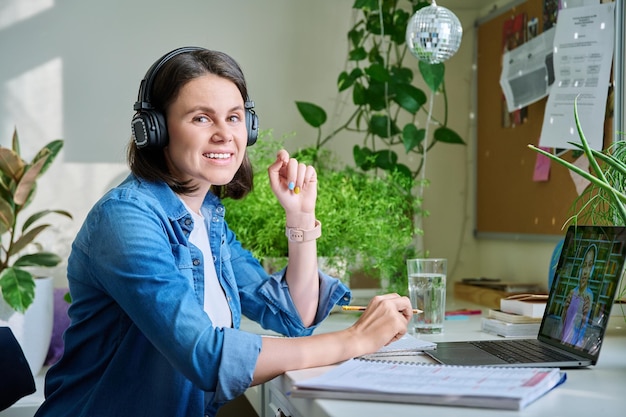 Portret van een lachende jonge vrouw in een koptelefoon met een laptop die naar de camera kijkt