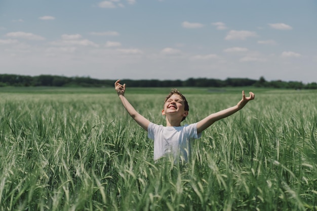 Portret van een lachende jongen in een wit T-shirt en spelend in een groen gerstveld Gelukkig kindjongen lachend en spelend in de zomerdag Kid die de natuur verkent Zomeractiviteit voor nieuwsgierige kinderen