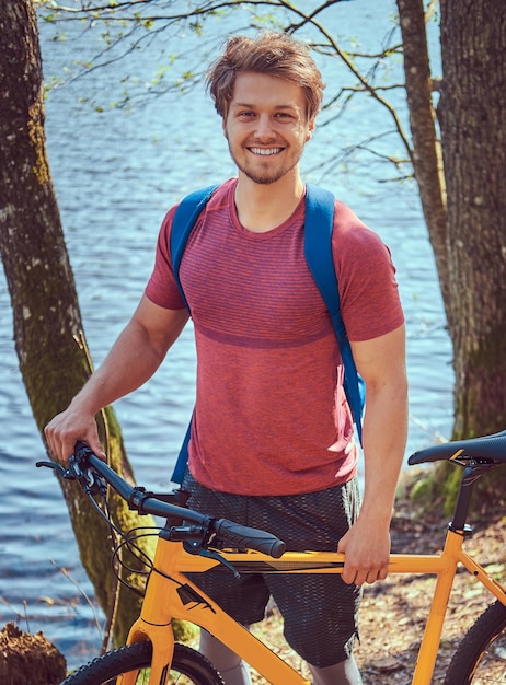 Portret van een lachende knappe man in sportkleding met een fiets. Ontspannen terwijl je aan het meer in het bos staat.