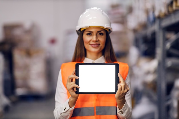 Portret van een lachende magazijnmanager die in een faciliteit staat met een tablet en deze laat zien