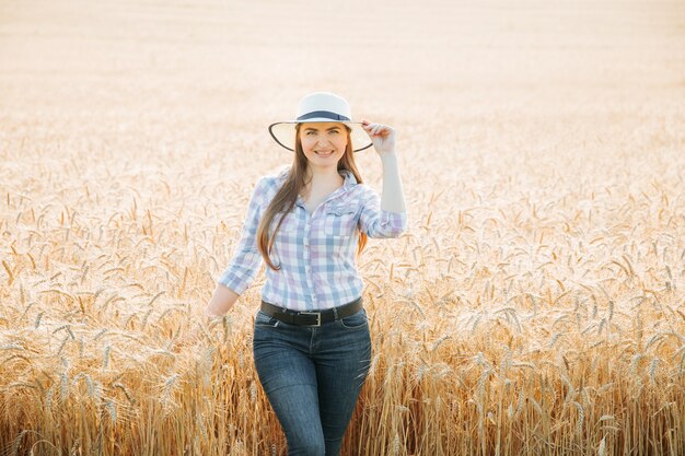 Portret van een lachende mooie en aantrekkelijke boerin met hoed is in het veld met gele ...