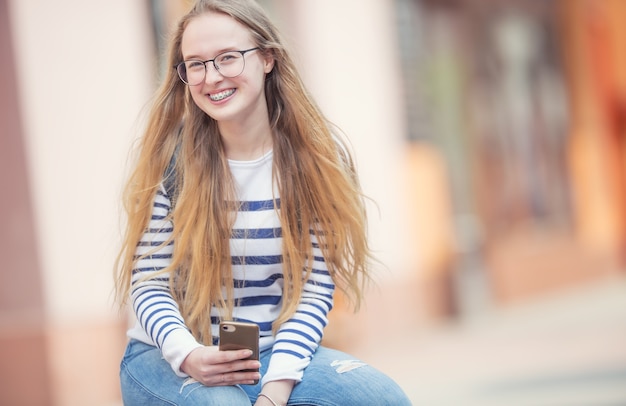 Portret van een lachende mooie tienermeisje met beugels. Jong schoolmeisje met schooltas en mobiele telefoon.