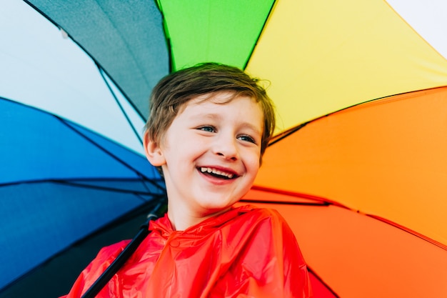 Portret van een lachende schooljongen met een regenboogparaplu achter een lachend kind houdt een kleurrijke paraplu vast