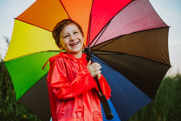 Portret van een lachende schooljongen met een regenboogparaplu in het parkkind houdt een kleurrijke paraplu vast