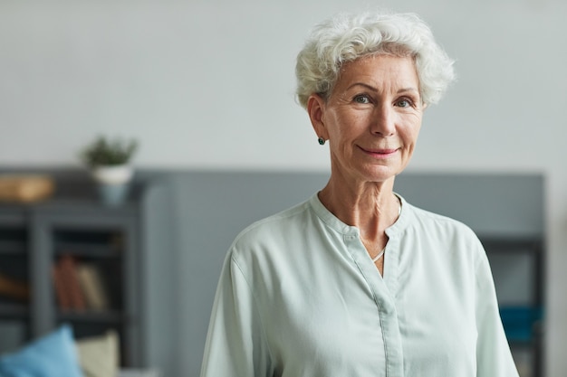 Portret van een lachende senior vrouw die naar de camera kijkt in de kopieerruimte van een bejaardentehuis