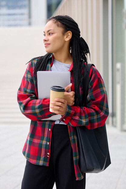 Portret van een lachende student die vanuit de klas door de straat loopt en een laptop vasthoudt