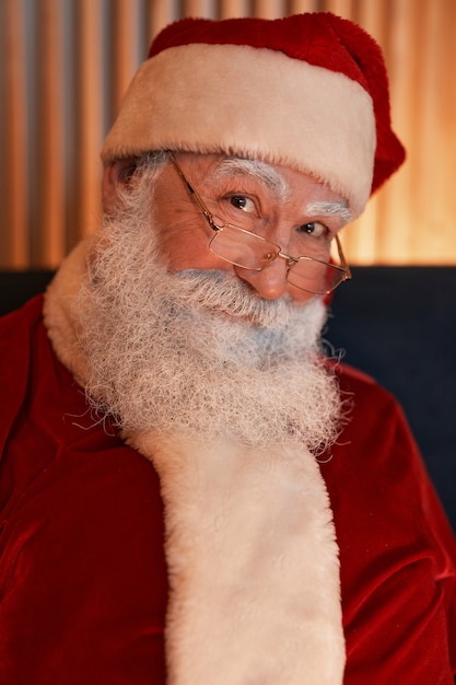 Portret van een lachende, vriendelijke senior witbaard kerstman in pet en bril met een rood kostuum