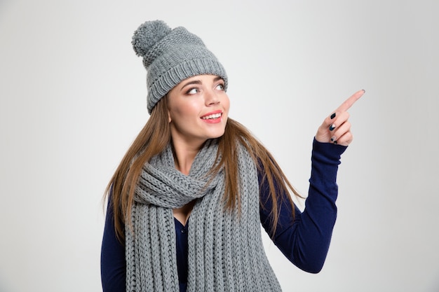 Portret van een lachende vrouw in winterdoek wijzende vinger weg geïsoleerd op een witte achtergrond a