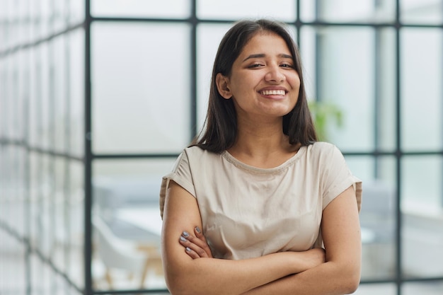 Portret van een lachende zakenvrouw met haar armen gekruist tegen de achtergrond van het kantoor