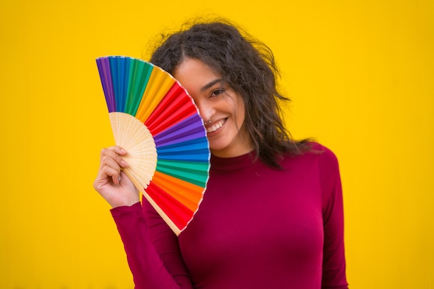 Portret van een latijns-vrouw die lacht met een regenboog lgbt-fan op een gele achtergrond