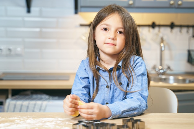 Portret van een leuk glimlachend meisje dat koekjesdeeg in de keuken voorbereidt. Kleine helper