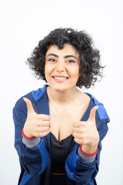 Portret van een leuke vrouw met krullend haar duimen opdagen.