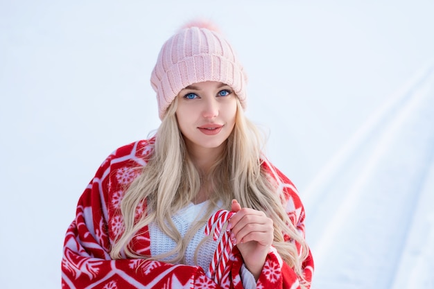 Portret van een leuke vrouw tegen de sneeuw in een roze hoed en rode plaid poseren voor de camera