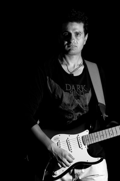 Foto portret van een man die gitaar speelt in een donkere kamer
