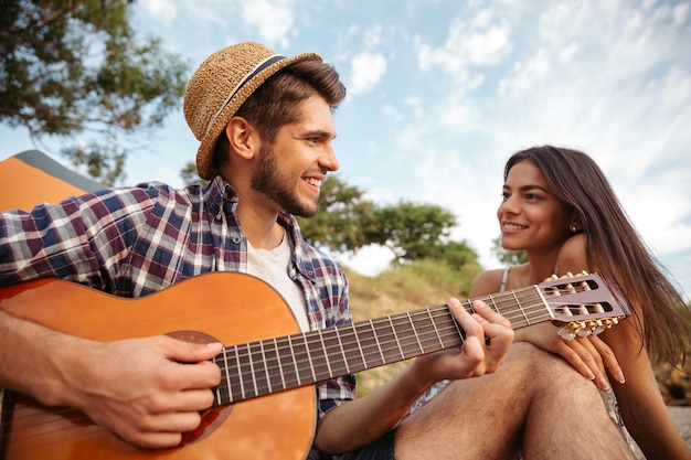 Portret van een man die gitaar speelt voor zijn vriendin die bij de campingtent zit