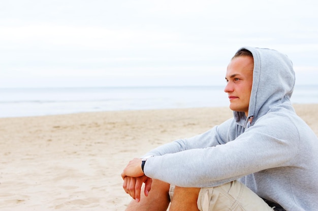 Portret van een man die in een jas op het strand zit