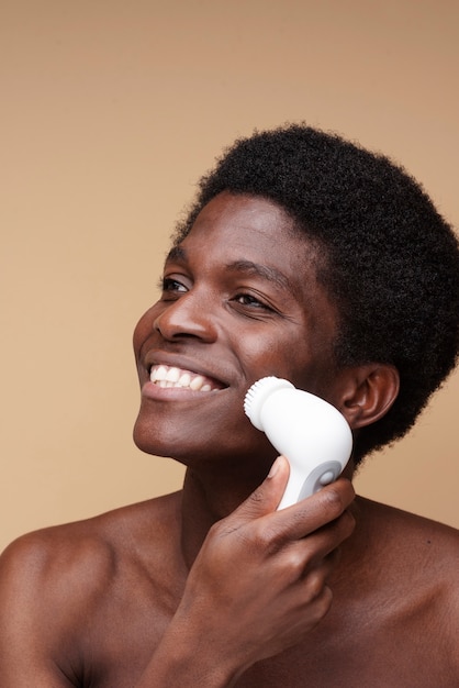 Portret van een man die lacht terwijl hij zijn gezicht schoonmaakt met een gezichtsborstel