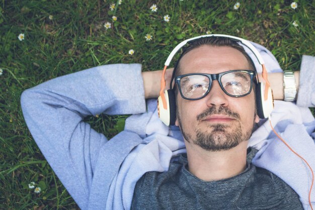 Foto portret van een man die naar muziek luistert terwijl hij op het gras ligt