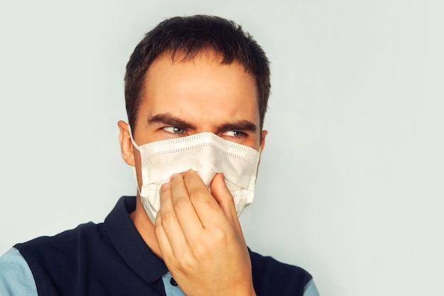 Portret van een man draagt een blauw medisch gezichtsmasker. blauwe achtergrond. Angst voor het coronavirus. onaangename geur. Zuur gezicht. walgelijke stank