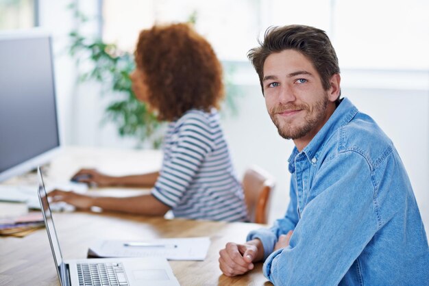 Portret van een man en een laptop in het kantoor aan het bureau met een glimlach en een mannelijke persoon die werkt of een technologisch apparaat voor het zoeken op het web Online computer en bedrijfscollega's samen en mensen die in de werkruimte zitten