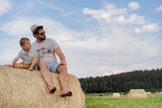 Portret van een man en zijn zoontje zittend op een ronde hooiberg in een groen veld op een zonnige zomerdag