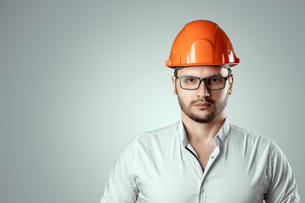 Portret van een man in een bouw oranje helm. Conceptenarchitectuur, bouw, techniek, ontwerp, reparatie. Ruimte kopiëren
