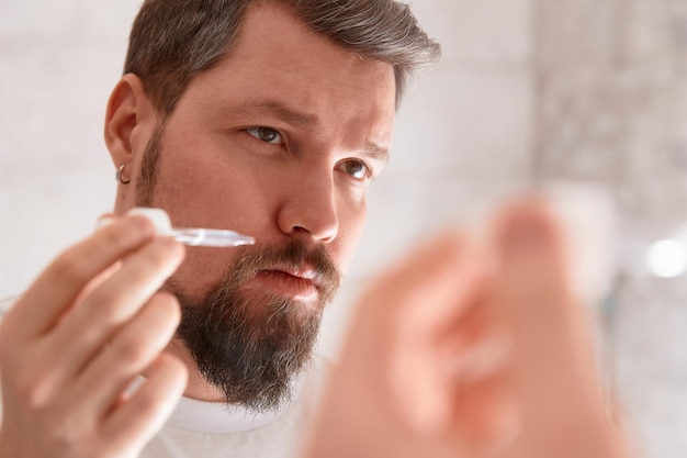 Portret van een man in een wit t-shirt die serum op zijn gezicht aanbrengt in de badkamer Zelfzorg ochtendprocedure