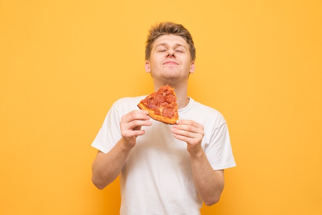 Portret van een man in een wit T-shirt eet een stuk verse pizza en krijgt een plezier