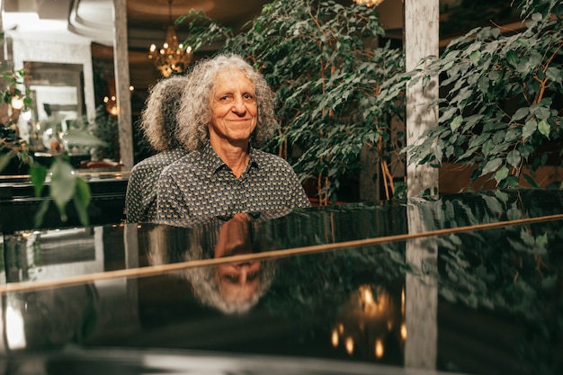 Portret van een man, leeftijd 60 - 65 jaar oud, grijs krullend haar, zittend aan de piano en een muziekstuk spelend, gefocust, zijaanzicht.