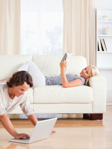 Portret van een man met behulp van een laptop, terwijl zijn vrouw is het lezen van een boek