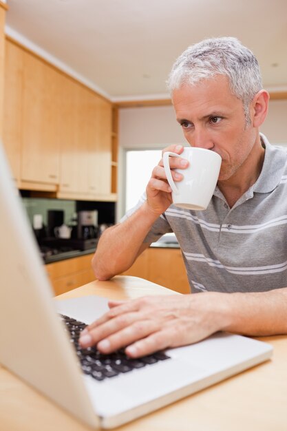 Portret van een man met behulp van een laptop tijdens het drinken van koffie