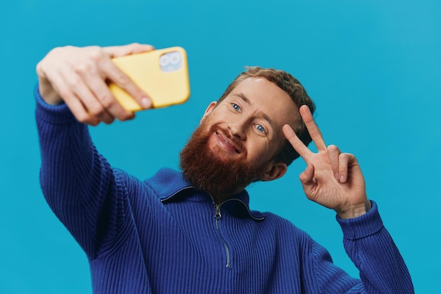 Portret van een man met een telefoon in zijn handen blogger neemt selfies op een blauwe achtergrond Communiceren online social media lifestyle