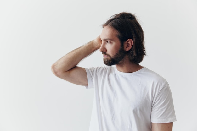 Portret van een man met een zwarte dikke baard en lang haar in een wit T-shirt op een witte geïsoleerde achtergrond emotie van verdriet en verlangen