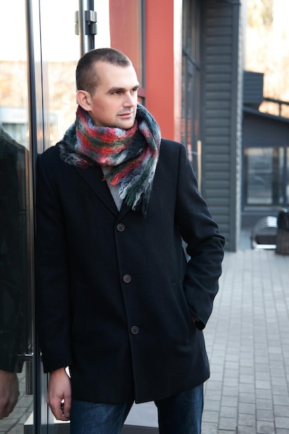 Portret van een man op straat in een gedrapeerde zwarte jas met een sjaal om zijn nek staand