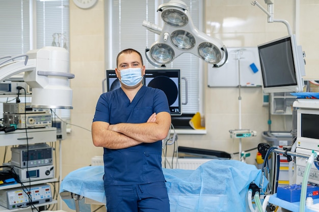 Portret van een mannelijke chirurg met masker staande armen gekruist in operatiekamer. Professionele en zelfverzekerde arts.