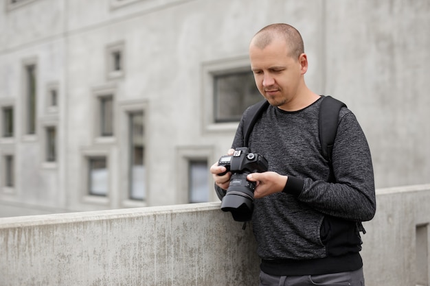 Portret van een mannelijke fotograaf of videograaf die video of foto's op zijn camera bekijkt over een betonnen gebouwachtergrond