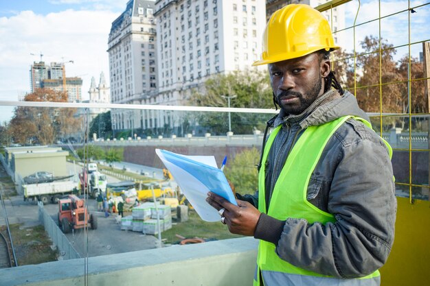 Portret van een mannelijke ingenieur van Afrikaanse etniciteit die op zijn werkruimte staat en naar de camera kijkt